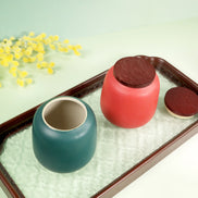 Aurora ceramic storage jars with wooden lids in coral and teal on decorative tray