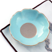 Turquoise ceramic tea strainer bowl with scalloped edge and gold rim on white cloth