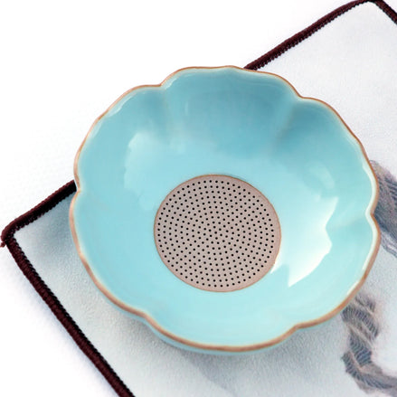 Turquoise ceramic tea strainer bowl with scalloped edge and gold rim on white cloth