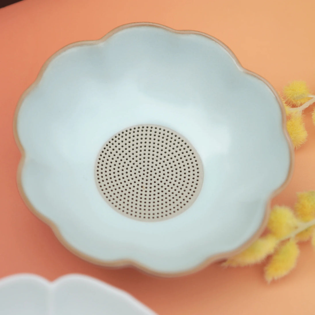Daisy-shaped silicone tea strainer in pale blue on coral background