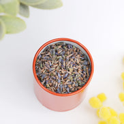 Dried lavender buds in pink tin container with orange lid, overhead view