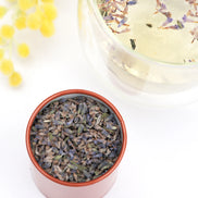 Dried lavender tea in pink ceramic bowl with glass teacup and yellow flowers