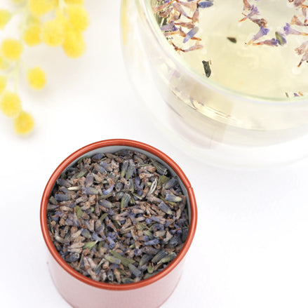 Dried lavender tea in pink ceramic bowl with glass teacup and yellow flowers