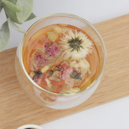 Floral tea with dried flowers in clear glass on timber board overhead view