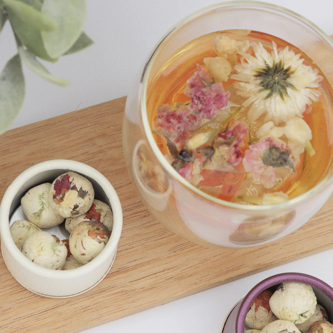 Herbal tea with floating dried flowers and botanicals in glass teacup on wooden board
