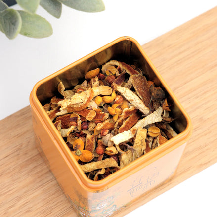 Orange tin filled with dried herbal tea blend on wooden surface