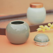 Jade ceramic jar with rose gold lid open on peachy surface with yellow flowers