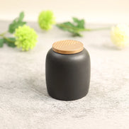 Kin Jar black ceramic storage container with gold rattan lid on concrete surface