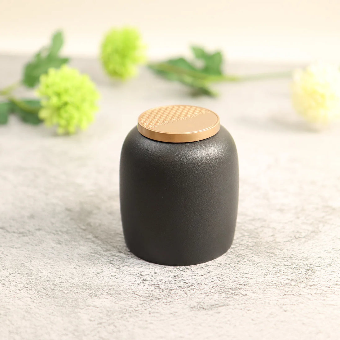 Kin Jar black ceramic storage container with gold rattan lid on concrete surface
