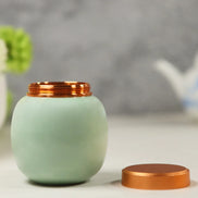 Mint green ceramic jar with copper lid beside tea pot and plant