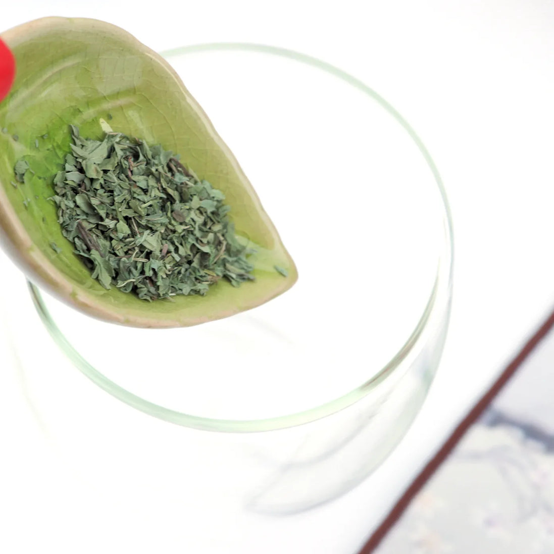 Loose leaf green tea in ceramic scoop over glass teacup