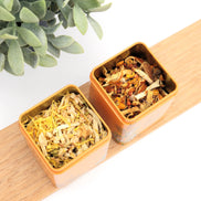 Two orange silicone containers filled with loose leaf herbal tea on wooden board