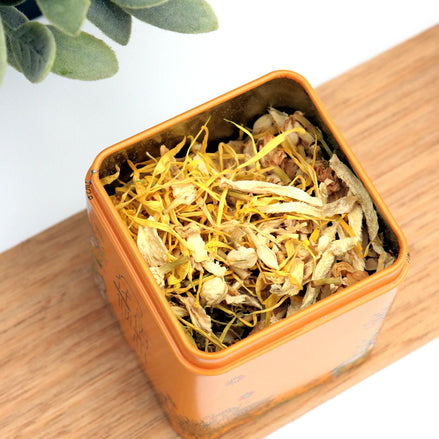 Orange storage tin filled with dried chamomile and calendula tea on timber surface