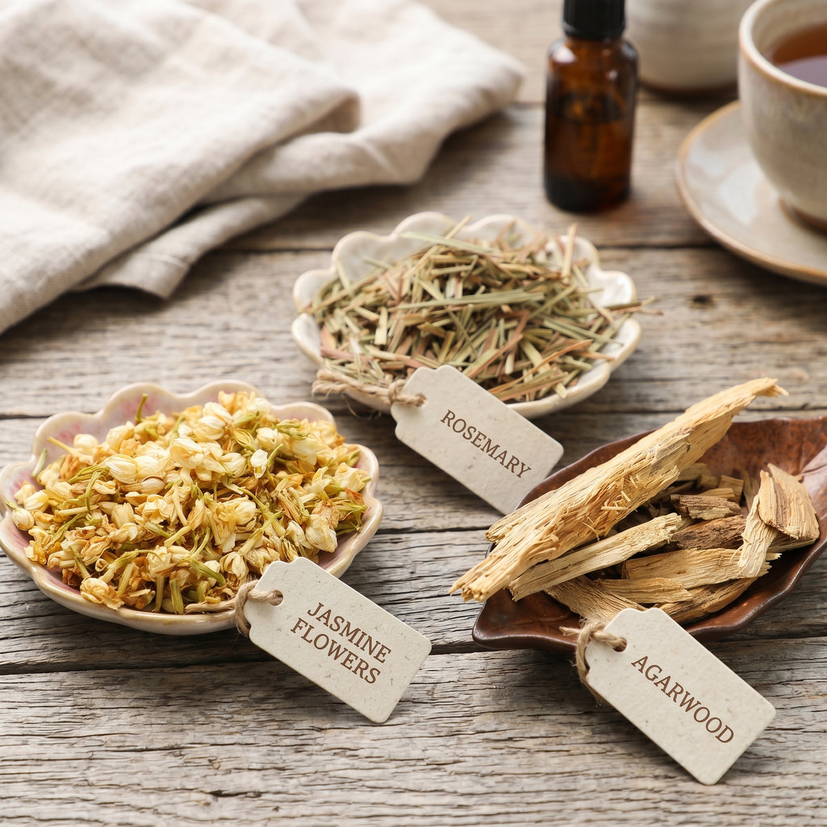 Herbal ingredients including jasmine flowers, rosemary, and agarwood on a wooden surface with labels.