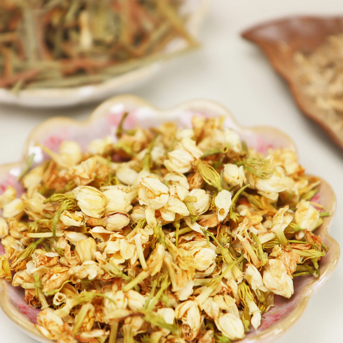 Dried whole jasmine flowers and petals displayed on decorative floral plate in cream and golden tones