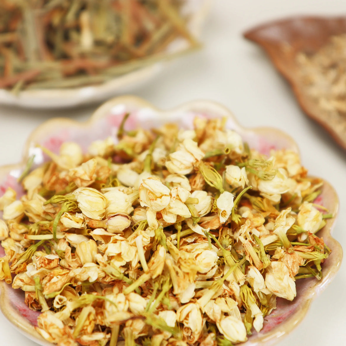 Dried whole jasmine flowers and petals displayed on decorative floral plate in cream and golden tones