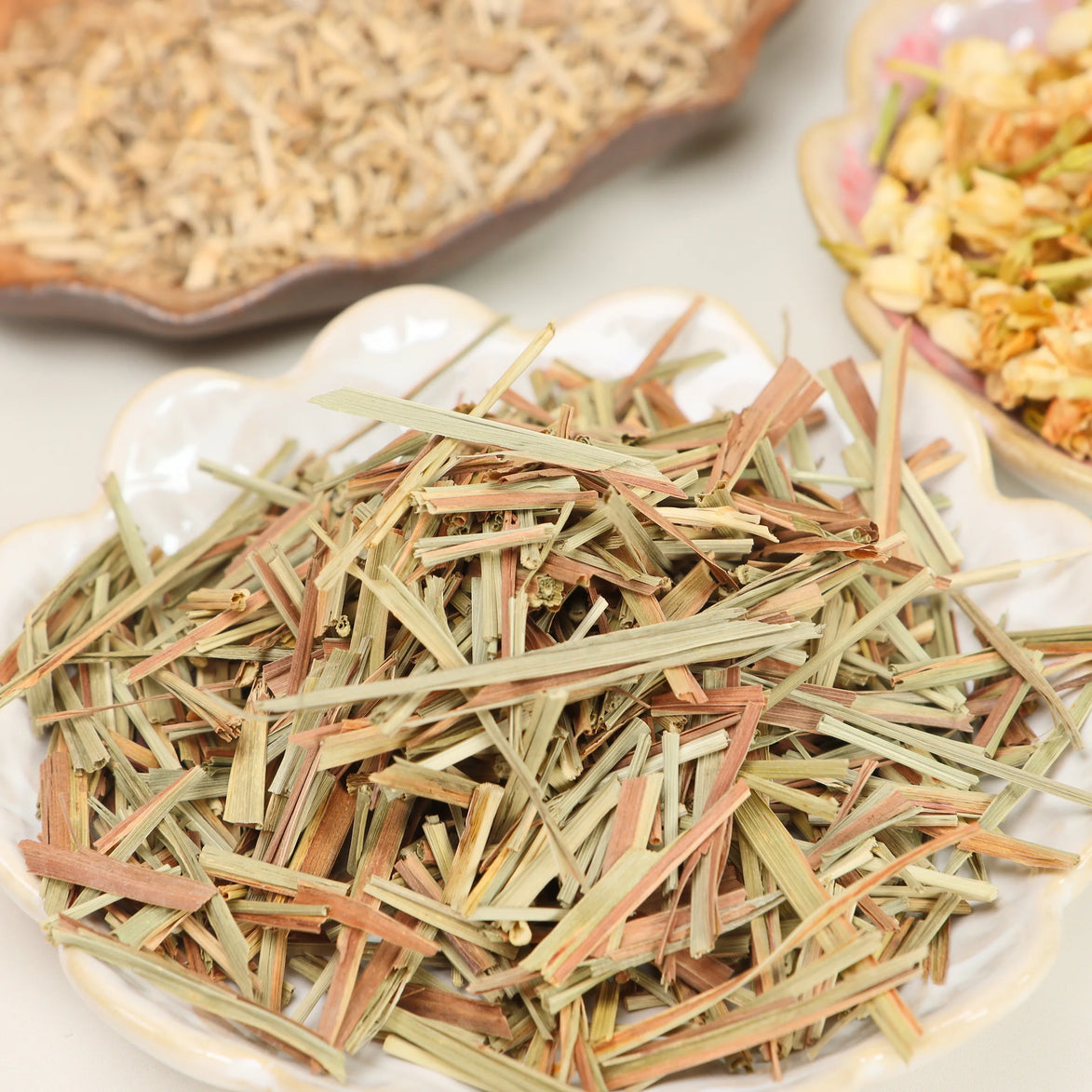 Dried lemongrass stalks in green and copper tones on white ceramic plate with herbal blends in background
