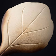 Cream ceramic burner with embossed leaf design and warm gradient lighting against black background