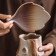 Hands holding leaf-shaped lid and tree stump ceramic aromatherapy burner in cream and brown tones