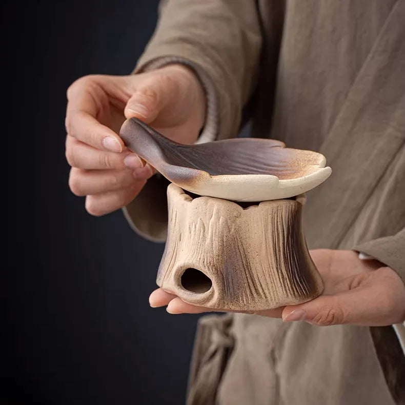 Hands holding ceramic woodland burner with tree stump base and gradient mushroom-shaped top in earth tones