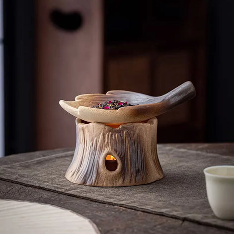 Ceramic woodland burner with tree stump base and leaf bowl containing colorful dried botanicals on wooden surface