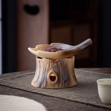 Ceramic woodland burner with tree stump base and leaf bowl containing colorful dried botanicals on wooden surface