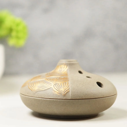 Grey ceramic incense burner with gold lotus petal design and ventilation holes on neutral background