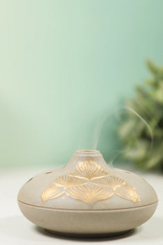 Grey ceramic incense burner with gold lotus petal design and matching base plate on white surface