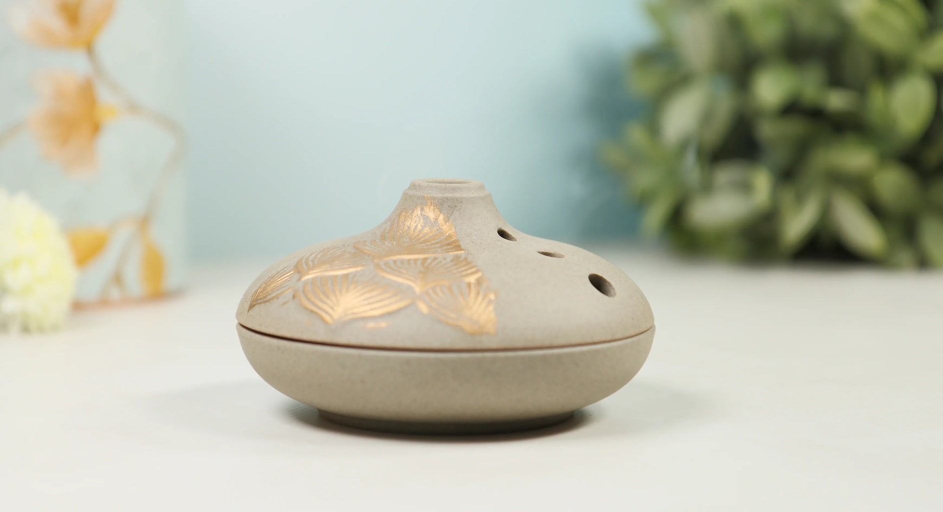 Grey ceramic incense burner with gold lotus petal pattern and vented dome top on white surface