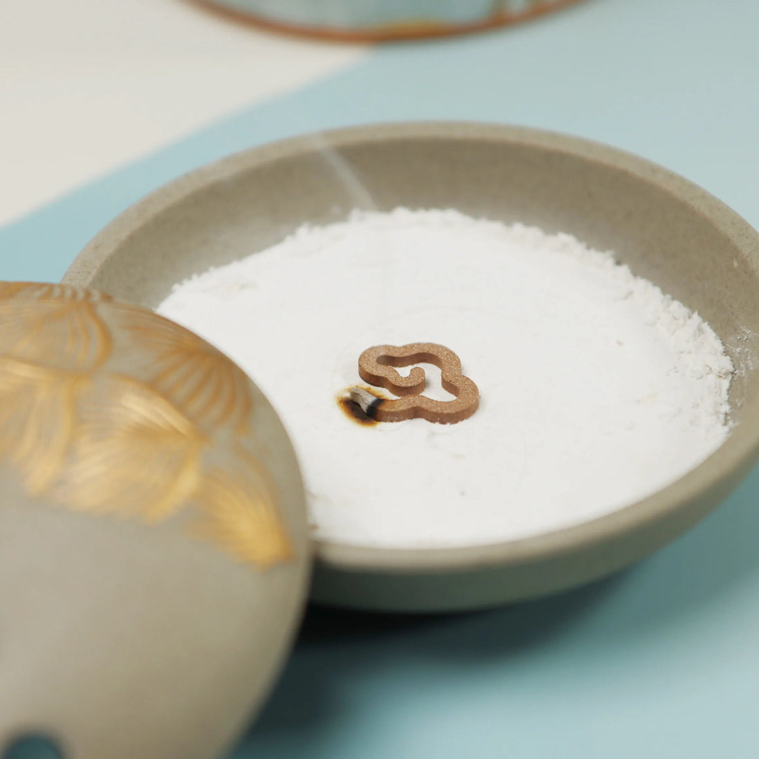 Grey ceramic incense burner with gold accents filled with white sand and heart-shaped incense holder