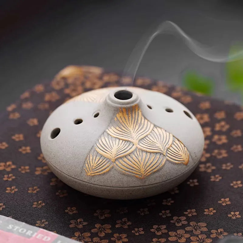 Grey ceramic dome incense burner with gold leaf pattern and ventilation holes releasing aromatic smoke