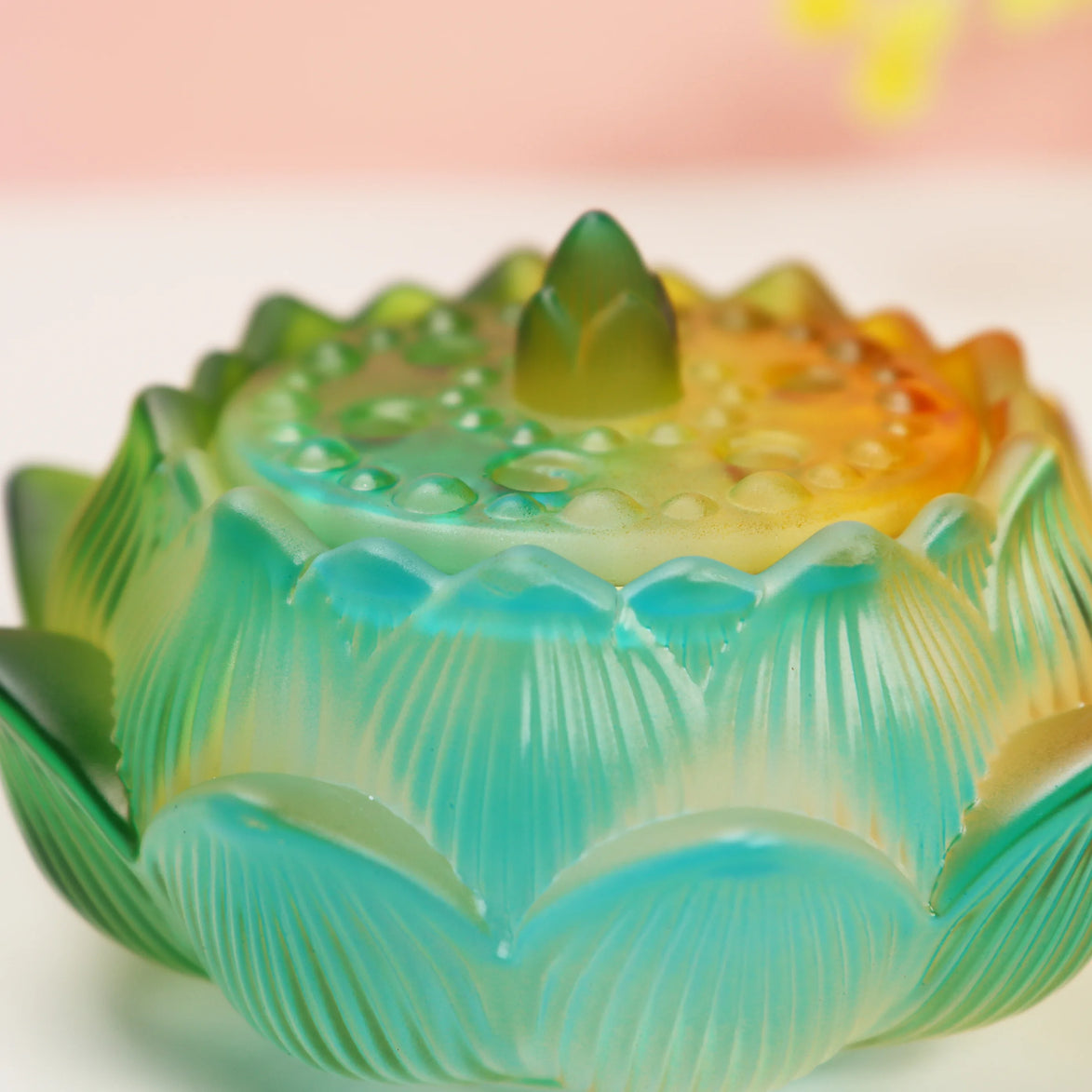 Turquoise to yellow ombre glass lotus burner with detailed petals and textured center on white surface