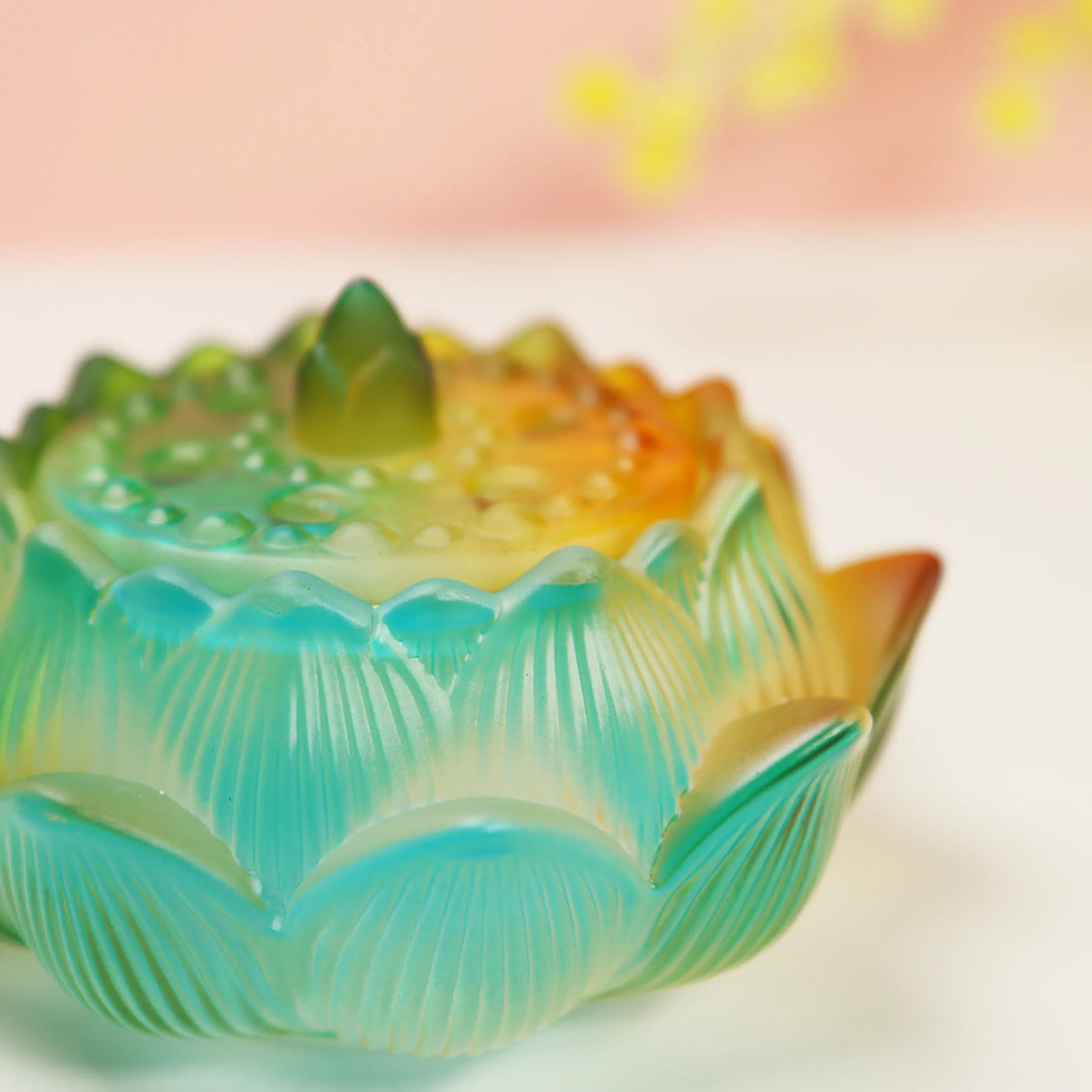 Turquoise to orange ombre glass lotus burner with detailed petals on white surface