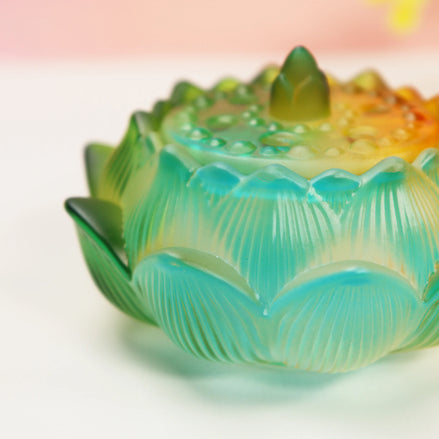 Turquoise to amber ombre glass lotus burner with detailed petal texture on white surface