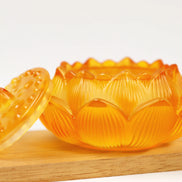 Amber lotus-shaped glass incense burner with textured petals and removable lid on wooden surface