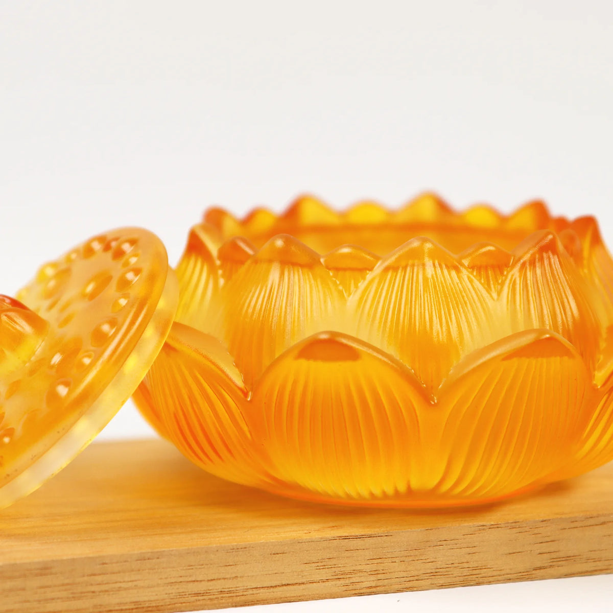 Amber lotus-shaped glass incense burner with textured petals and removable lid on wooden surface