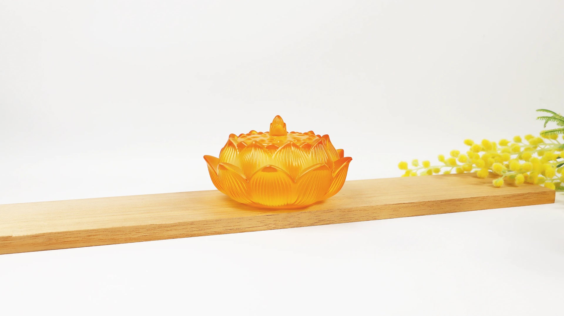 Amber translucent glass lotus flower incense burner with carved petals and ornate lid on wooden surface