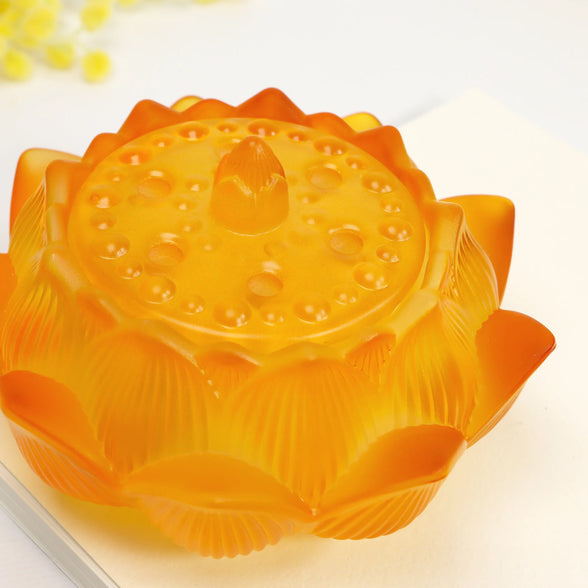 Translucent amber glass lotus flower incense burner with carved petals and textured details on white surface