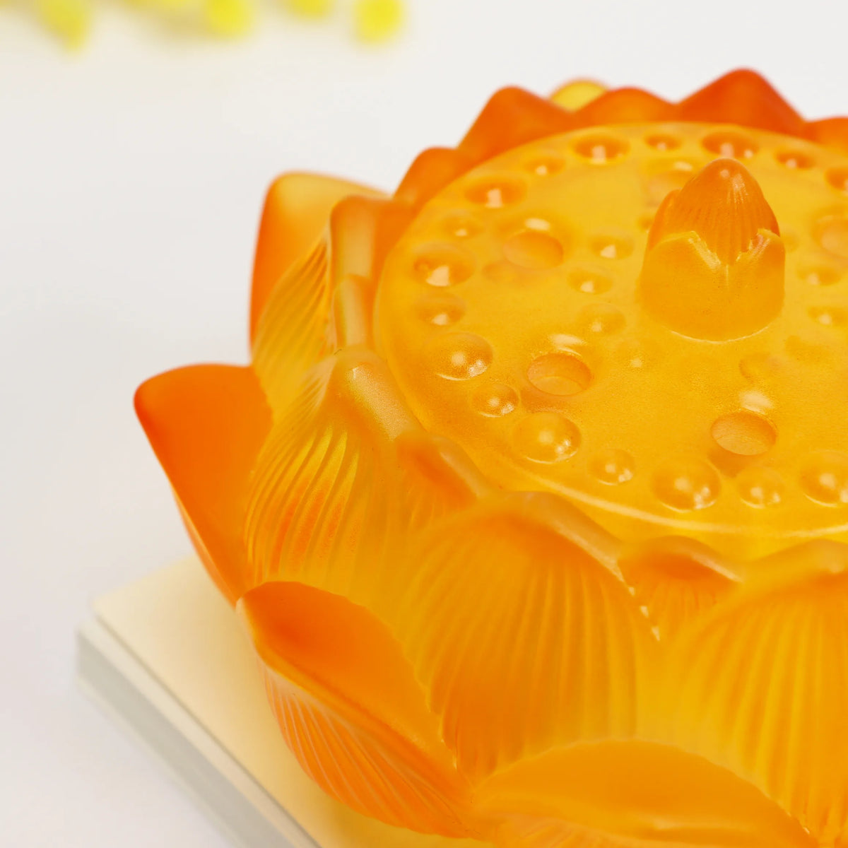 Amber glass lotus flower incense burner with layered petals and textured surface on white display stand