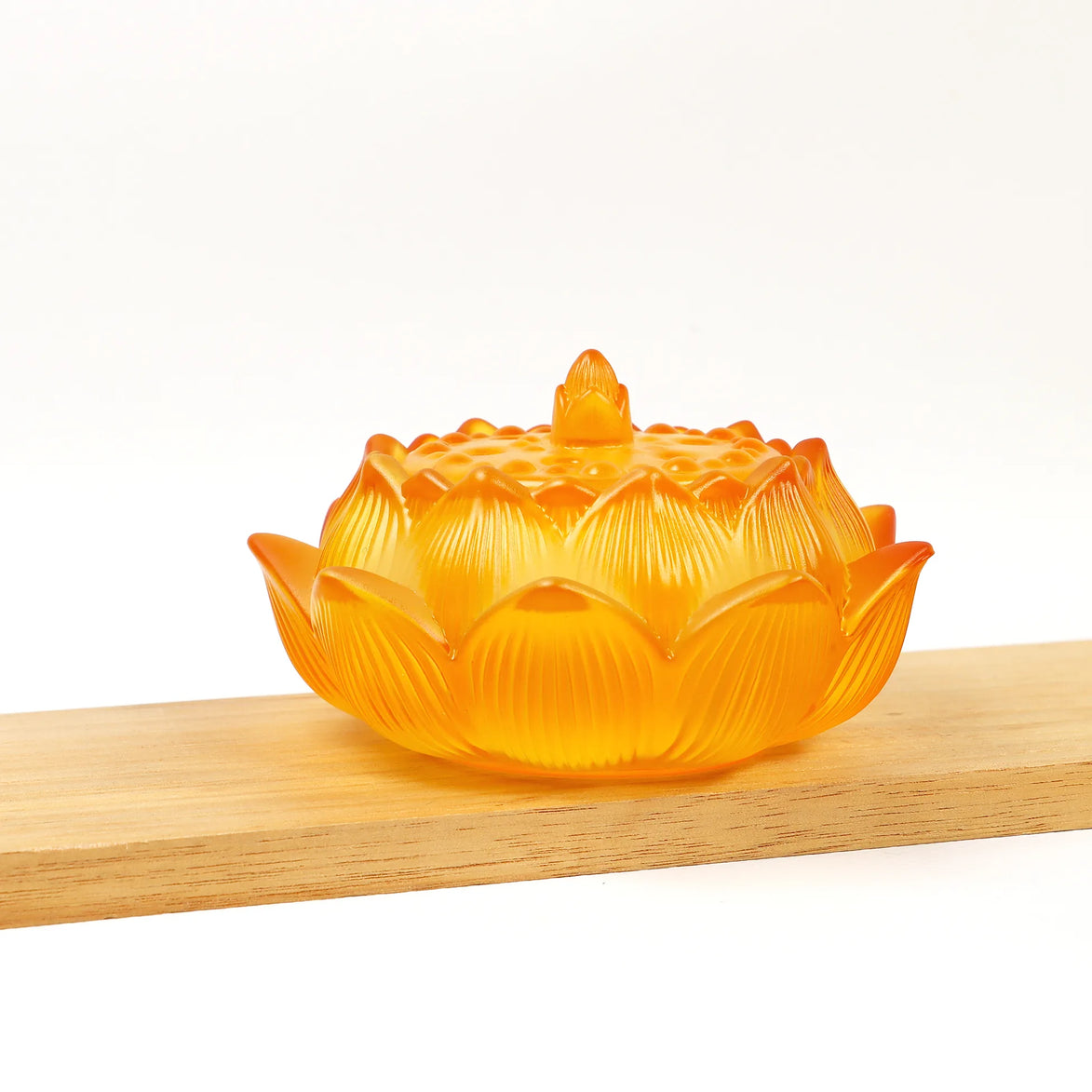 Amber translucent glass lotus flower incense burner with detailed petals and sealing lid on wooden surface