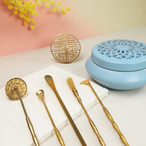 Blue ceramic incense burner with lattice lid alongside gold brass tools and decorative seal molds on white surface