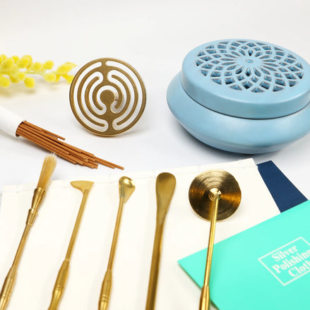 Blue ceramic incense burner with lattice lid, brass seal mold, and gold wax sealing tools on white surface