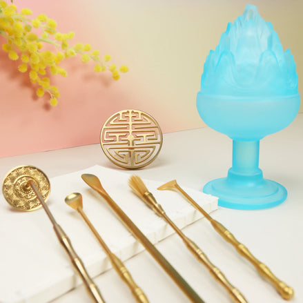 Blue frosted glass Boshan incense burner with brass tools, seal mold, and palo santo sticks on white surface