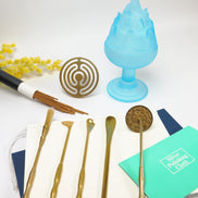 Blue glass Boshan incense burner with brass ritual tools and circular gold seal on white surface with yellow flowers