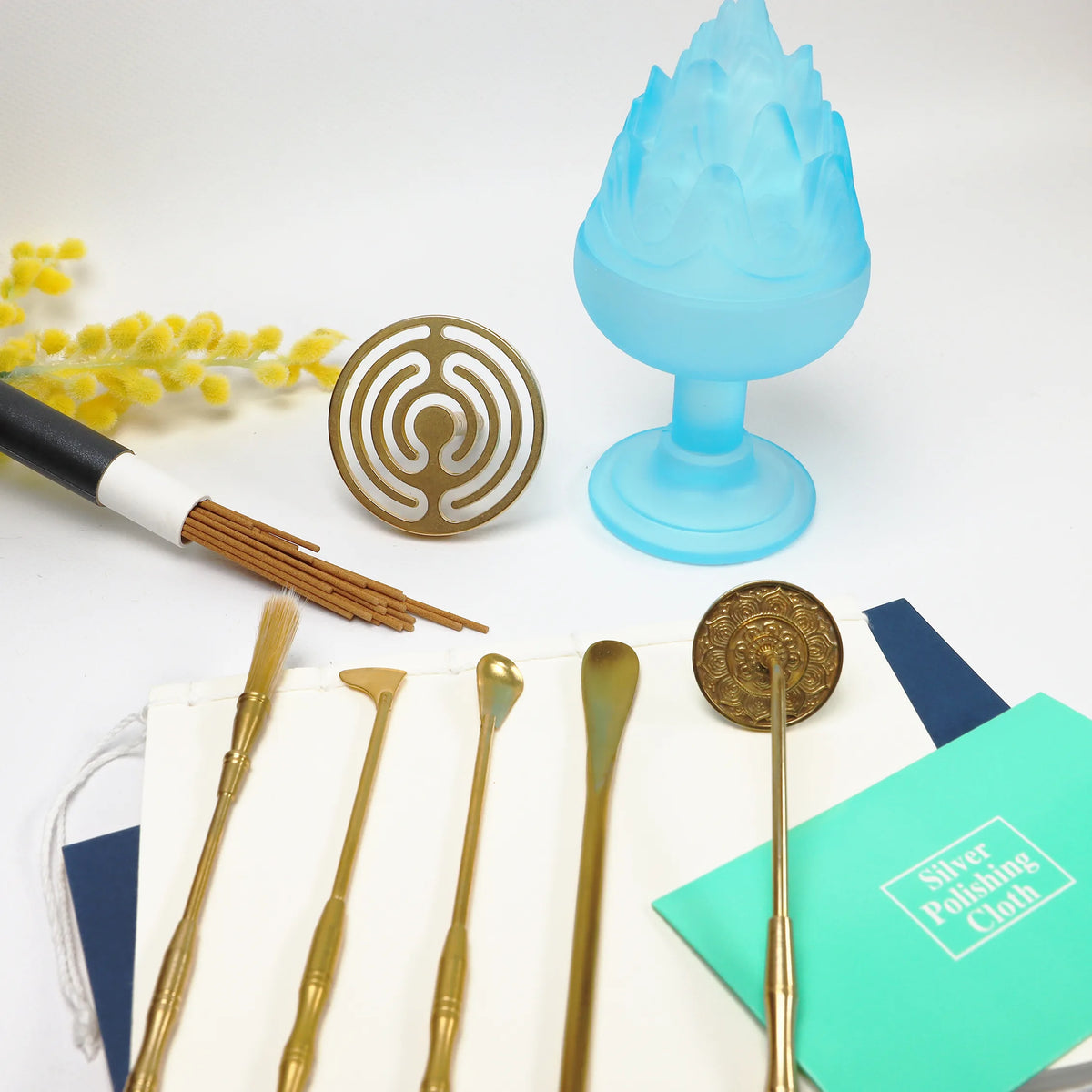 Blue glass Boshan incense burner with brass ritual tools and circular gold seal on white surface with yellow flowers