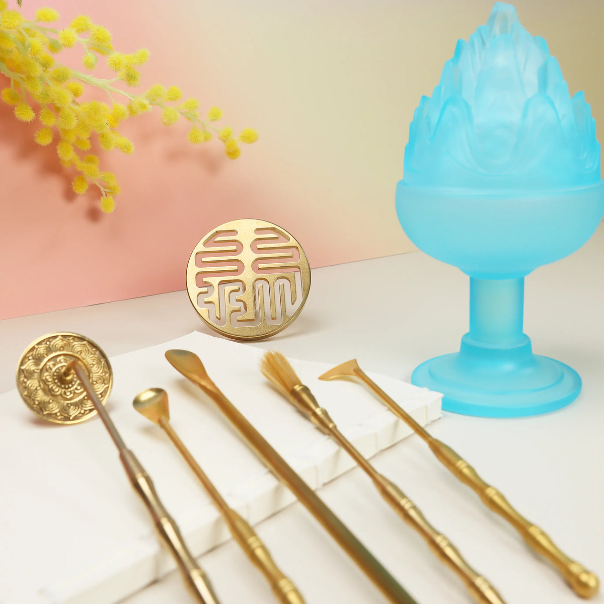 Blue glass boshan incense burner with brass lotus seal mold and five gold crafting tools on white surface