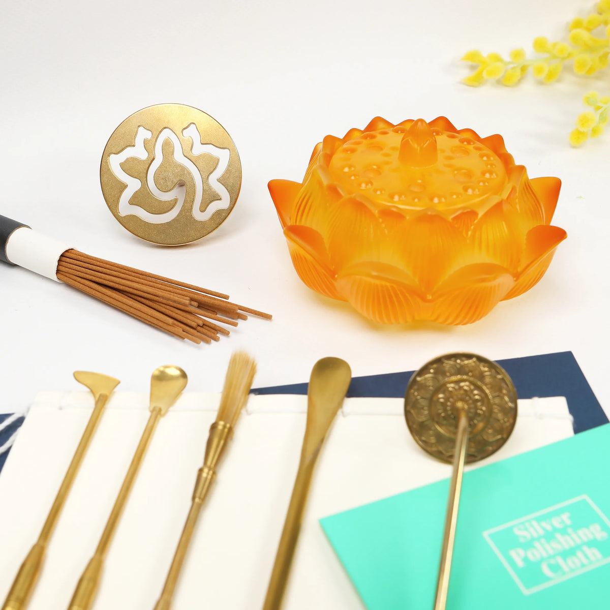 Amber glass lotus-shaped incense holder with brass tools and decorative seal stamps on white surface