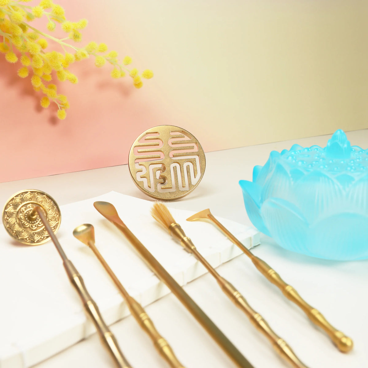 Brass prosperity seal with five gold tools and translucent blue lotus holder on white marble surface