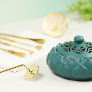 Teal ceramic incense burner with ornate lattice lid and lotus petal base, displayed with gold incense tools
