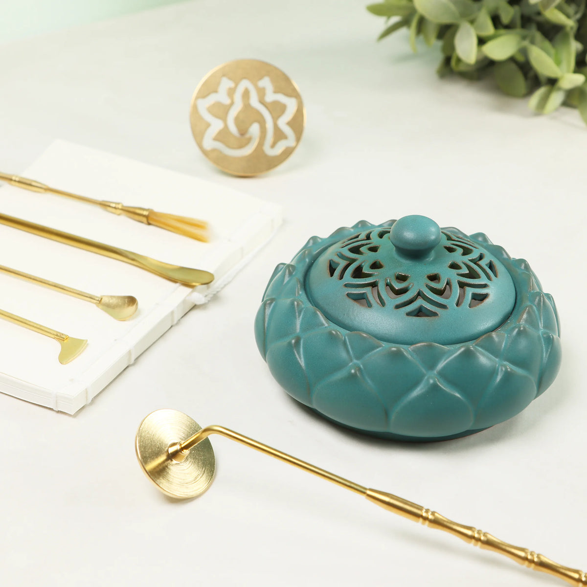 Turquoise ceramic incense burner with ornate cutout design alongside gold brass sealing tools and white mold
